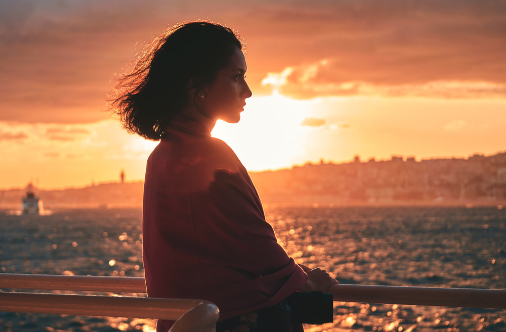 beautiful woman standing on deck of cruise ship and looking away at sunset.